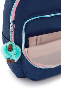 Zaino navy con la tasca frontale aperta, interno rosa chiaro, zip turchese e un portachiavi a forma di scimmia blu in peluche attaccato.