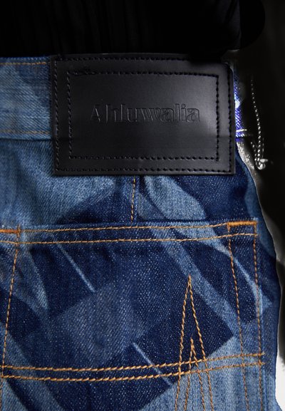 Jeans iz denima z usnjenim oznako "Ahluwalia" v odtisnjenem formatu. Modre odtenke s kontrastnimi zlatimi šivi in geometrijskimi vzorci.