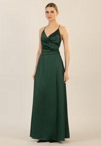 Grünes Satin-Maxikleid mit Wickeldesign, dünnen Trägern und einem Seitenschlitz. Glatte Textur mit einem sanften Glanz, der Eleganz und Drapierung zur Schau stellt.