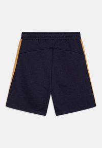 Marinblå shorts med elastisk midja och senapsgula sidostrickor, visade bakifrån på en vit bakgrund.
