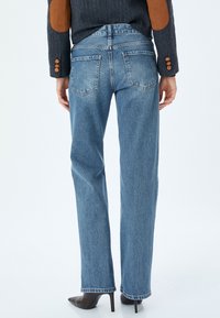 Vaqueros de tiro alto rectos de color azul claro con un diseño clásico de cinco bolsillos y un ligero desgaste. El material es denim resistente con costuras visibles.