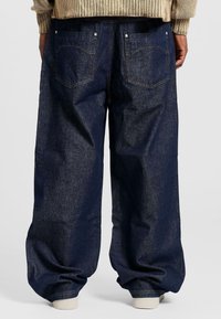 Pantaloni in denim di un blu indaco scuro, con vestibilità ampia, design a cinque tasche e cuciture a contrasto. La texture è leggermente robusta.