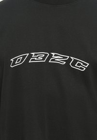 Un t-shirt en coton noir présente un grand texte courbé en blanc, audacieux, "D32C" sur le devant, avec une texture douce et un design à col ras du cou.