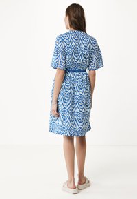 Blå mönstrad klänning med korta puffärmar, ett bälte som framhäver midjan och en avslappnad passform. Slät tyg med en livlig geometrisk design.