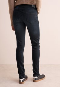 Jeans skinny blu scuro in denim, dotati di due tasche posteriori e un design a vestibilità slim. Outfit completato con sneakers scure e un maglione beige.