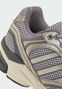 Gray athletic shoe featuring mesh upper, metallic accents, textured rubber sole, and layered design with supportive heel and lacing system.