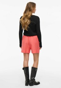 Koralfarvede shorts med elastisk talje, parret med en tætsiddende sort sweater og knæhøje sorte støvler, set fra ryggen.