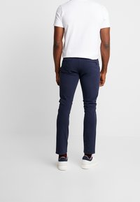 Granatowe, dopasowane spodnie o gładkiej fakturze, z dwoma tylnymi kieszeniami i detalem z zamkiem błyskawicznym, zestawione z białą koszulą z krótkim rękawem i sneakersami.