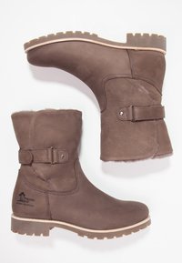 Botas de tobillo de cuero marrón con un interior suave forrado de piel de fur, detalle de hebilla y suela de goma texturizada. Presenta un diseño cosido.