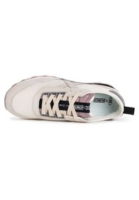 Zapatilla beige con un upper liso y texturizado, acentos grises, lengüeta en un tono rosa pálido y cordones planos. Presenta una etiqueta de logo negra en el costado.