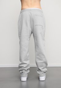 Pantaloni de trening gri deschis, dintr-un material moale, cu talie elastică, croi lejer și un singur buzunar pe spate. Pantofi albi cu tălpi texturate.