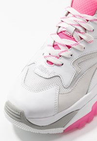 Baskets blanches et grises avec une tige en mesh, des accents roses et une semelle en caoutchouc texturée. Les lacets sont blancs avec des rayures roses. Logo sur le côté.