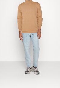 Ljusa bruna turtleneck-tröja i strukturerad tyg, matchad med ljusblå raka jeans och grå sneakers med svarta detaljer.