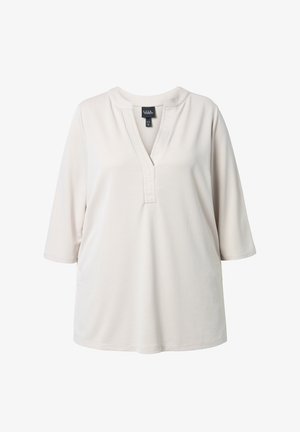 Kermanvalkoinen pitkähihainen paita, jossa on pyöreä pääntie ja V-muotoinen halkio, jossa on ommellut pystysuuntaiset laskokset.