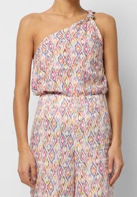 Asymmetrisk top i let, mønstret stof med et flerfarvet diamantdesign. Glat tekstur med en dekorativ knude og knaplukning.