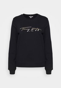 Černá mikina vyrobená z měkké bavlny, s metalickým stříbrným textem loga "Tommy Hilfiger est. 1985" na přední straně a žebrovanými manžetami.