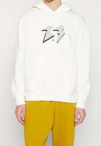 Felpa bianca con cappuccio e tasca a canguro anteriore, caratterizzata da un design di fulmine grigio e il logo Jordan stampato al centro. Tessuto morbido, vestibilità rilassata.