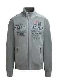 Graue Zip-Up-Jacke mit strukturierten Ärmeln, hohem Kragen und seitlichen Taschen; mit gedrucktem Text und Grafiken in Schwarz und Rot.