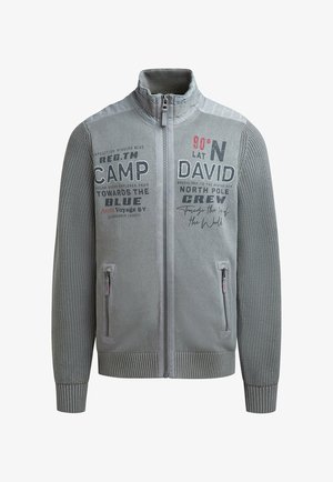 Graue Zip-Up-Jacke mit strukturierten Ärmeln, hohem Kragen und seitlichen Taschen; mit gedrucktem Text und Grafiken in Schwarz und Rot.