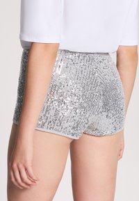 Shorts di paillettes argento con un design aderente. Il capo presenta paillettes luccicanti disposte verticalmente e una morbida vita elastica.