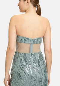 Een mintgroene strapless jurk met ingewikkelde kralenwerk en pailletten, met een doorschijnende achterkant en een getailleerd silhouet.