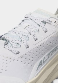 Κοντινό πλάνο ενός λευκού αθλητικού παπουτσιού με κορδόνια με σχέδιο, διάτρητες πλευρές και τη σήμανση «ALTRA» στη μεσαία σόλα.