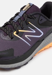 Fialovo-černá sportovní obuv s hálkovým svrškem, reflexními prvky, polstrovaným límcem a texturovanou podrážkou. Má kontrastní oranžovou podrážku.