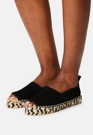 Czarne espadryle zamszowe z odkrytymi palcami, z plecioną podeszwą z juty z czarnymi i naturalnymi paskami, spoczywające na teksturowanej powierzchni.