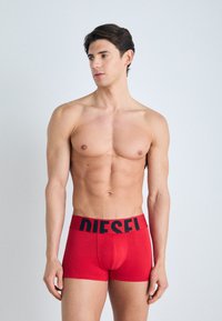 Boxer-culottes en coton rouge avec un logo "DIESEL" noir sur la ceinture. Design ajusté avec une texture lisse et une longueur de jambe courte.