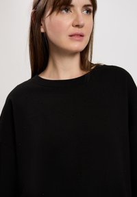 Czarna dzianinowa bluza z luznym fasonem, szerokim dekoltem i małymi zdobieniami, które nadają jej dodatkowej tekstury.