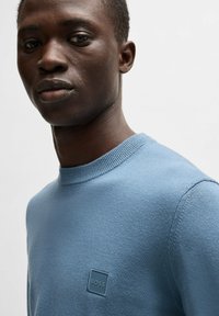 Helles blaues, Rundhals-Pullover aus weichem Strickstoff. Verfügt über ein kleines quadratisches Logo-Tag auf der linken Brust. Glatte Textur, taillierte Passform.