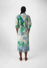 Genomskinlig blommig kimono i grön, gul och blå med korta ärmar och en mittknut, med ett detaljerat mönster i kanten.