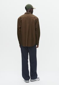 Bruin gestreept longsleeve shirt met een relaxed fit, gecombineerd met marineblauwe wijde broek en grijze sneakers, aangevuld met een groene pet.
