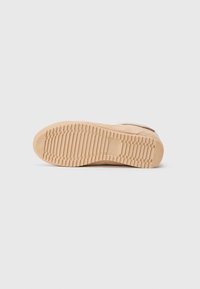 Semelle de sneaker beige avec un motif de traction en caoutchouc texturé, présentant une légère courbe et des bords biseautés pour le confort et le soutien.