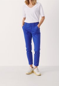 Blauwe katoenen broek met taps toelopende pijpen, zijzakken en een platte voorkant, gecombineerd met een witte v-hals t-shirt en witte sneakers.