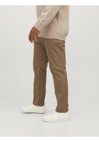Pantaloni di cotone marroni a taglio slim, con dettagli di cuciture visibili, abbinati a sneakers bianche. Maglione con polsini a costine e design rilassato.