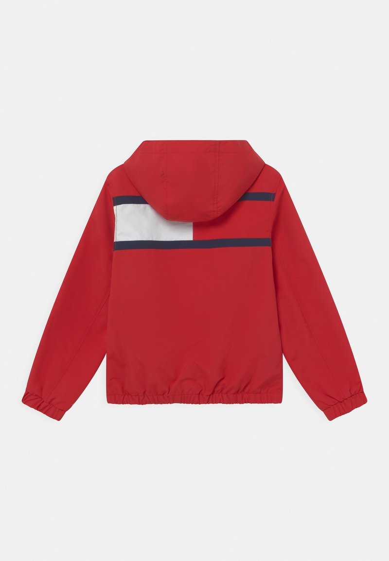 Rød hættejakke med elastiske manchetter, der har et hvidt og marineblåt vandret stribemønster på ryggen og en indsnævret talje.