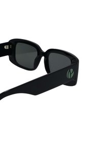 Čierne slnečné okuliare s obdĺžnikovým tvarom, sivými šošovkami a elegantným rámom. Na stranách sa nachádza zelený detail loga.