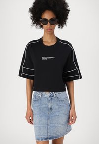 Melnas īsās sporta jakas ar baltu apdari un "KARL LAGERFELD JEANS" logotipu. Apvienota ar gaiši zilu džinsu svārku ar teksturētu rakstu.
