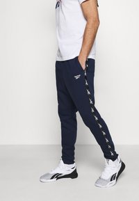 Námořnické modré sweatpants s bočními pruhy, které mají černo-bílý geometrický vzor, vyrobené z měkké látky, s elastickým pasem a bočními kapsami.