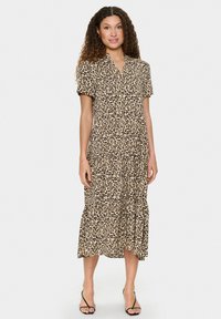 Robe midi imprimée léopard en tissu léger ; manches courtes, décolleté en V, design à volants, beige avec taches marron, portée avec des sandales noires.