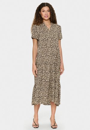 Leopardenmuster Midi-Kleid aus leichtem Stoff; kurze Ärmel, V-Ausschnitt, gestufter Rock, beige mit braunen Flecken, getragen mit schwarzen Sandalen.