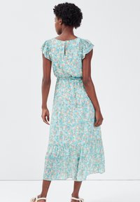 Robe florale avec un fond turquoise clair, manches courtes à volants, taille cintrée et ourlet à étages. Présente un détail en forme de trou de serrure au dos.