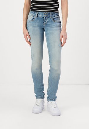 Skinny jeans in light blue denim with a faded finish, featuring a five-pocket design and dual button fly, paired with white sneakers.
