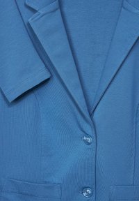 Chaqueta azul con un diseño clásico, incluye solapas, dos botones y dos bolsillos delanteros; confeccionada con tela texturizada y acabado suave.