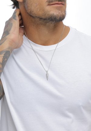 Silver chain necklace features a textured, elongated pendant. Worn over a plain white t-shirt, accentuating minimalist design.