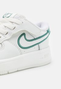 Balti Nike sportbačiai su žaliu siuvinėjimu, tekstūruota balta padas, raišteliai ir tinklelio pamušalas. Siuvinėta dizainas ir lygus odos paviršius.