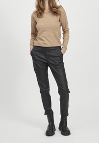 Beige long-sleeve knit sweater paired with black leather pants and black ankle boots. Pants feature side pockets and a slim fit.