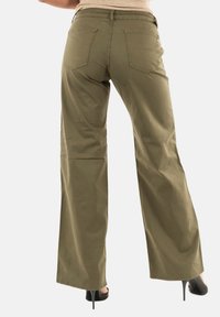 Pantaloni a gamba larga verde oliva in cotone, dotati di due tasche posteriori e una finitura liscia, abbinati a scarpe con tacco nere.