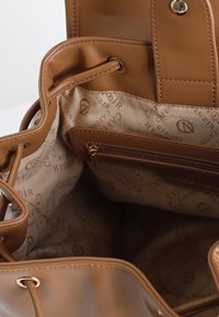 Brun läderhandväska med en mjuk yta, med ett foder av tyg tryckt med varumärkeslogotypen, en dragkedjeficka och justerbara remmar.